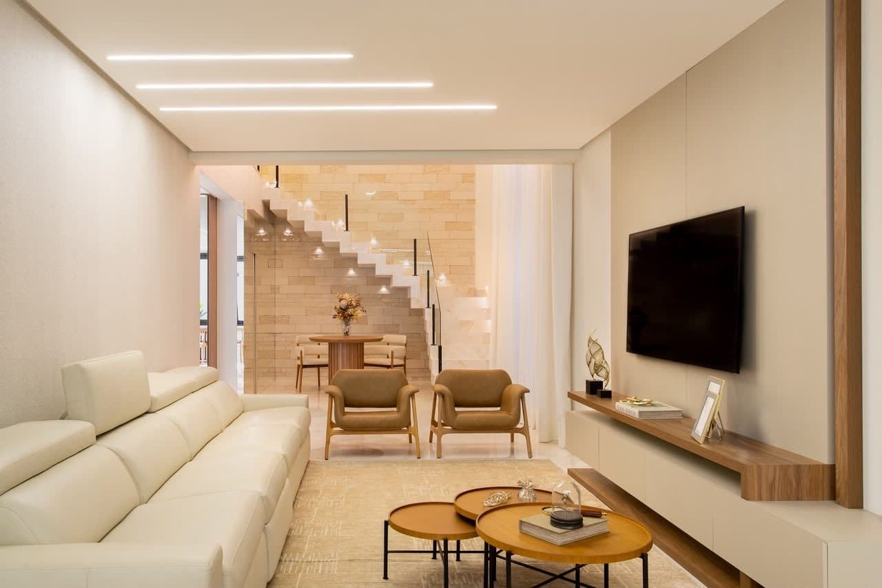 Sala finalizada e clara, com escada em pedra, sofá off-white e poltronas em palha