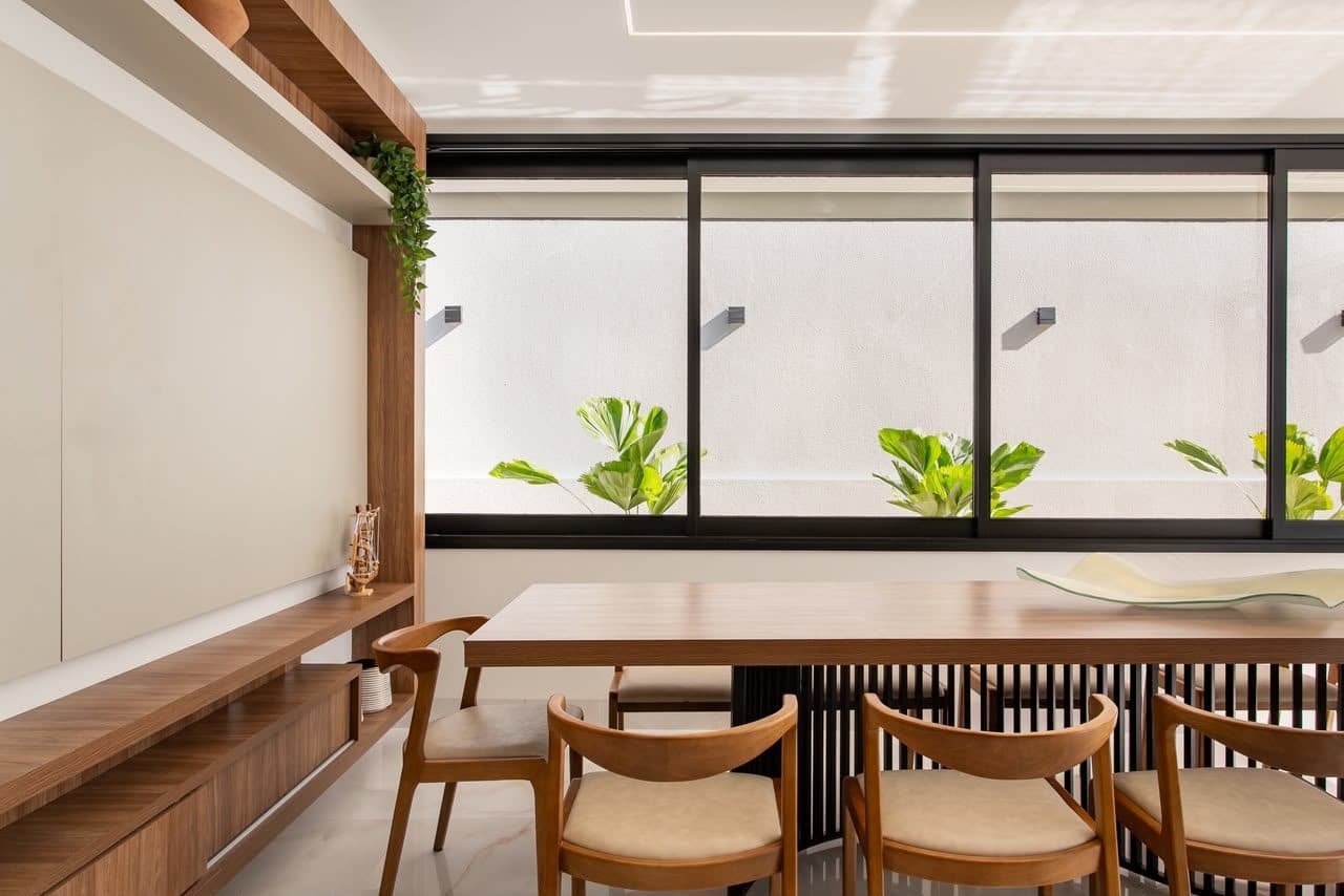 Sala de jantar residencial com mesa de madeira maciça e esquadrias pretas