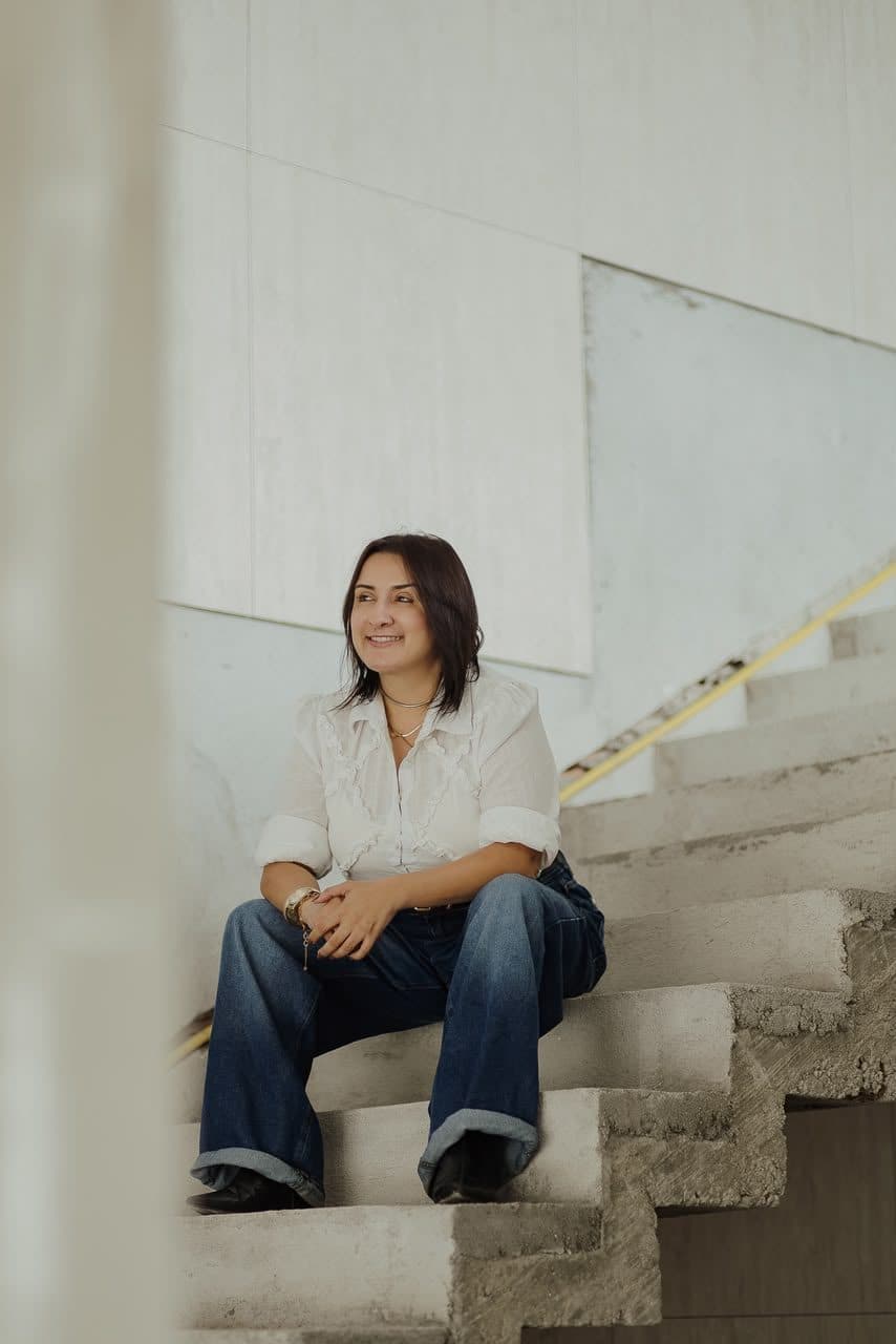 Cristiane Fonseca, arquiteta e urbanista, sentada em uma escada de projeto em ambiente claro